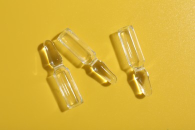 Photo of Glass ampoules with liquid on yellow background, flat lay