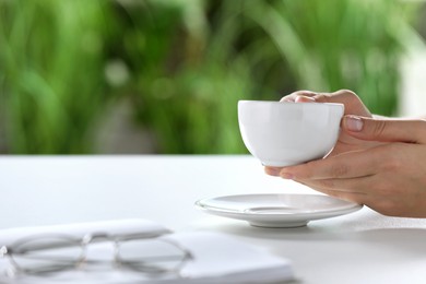 Photo of Woman holding cup of coffee at white table indoors, closeup