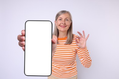 Happy mature woman showing mobile phone with blank screen on white background. Mockup for design