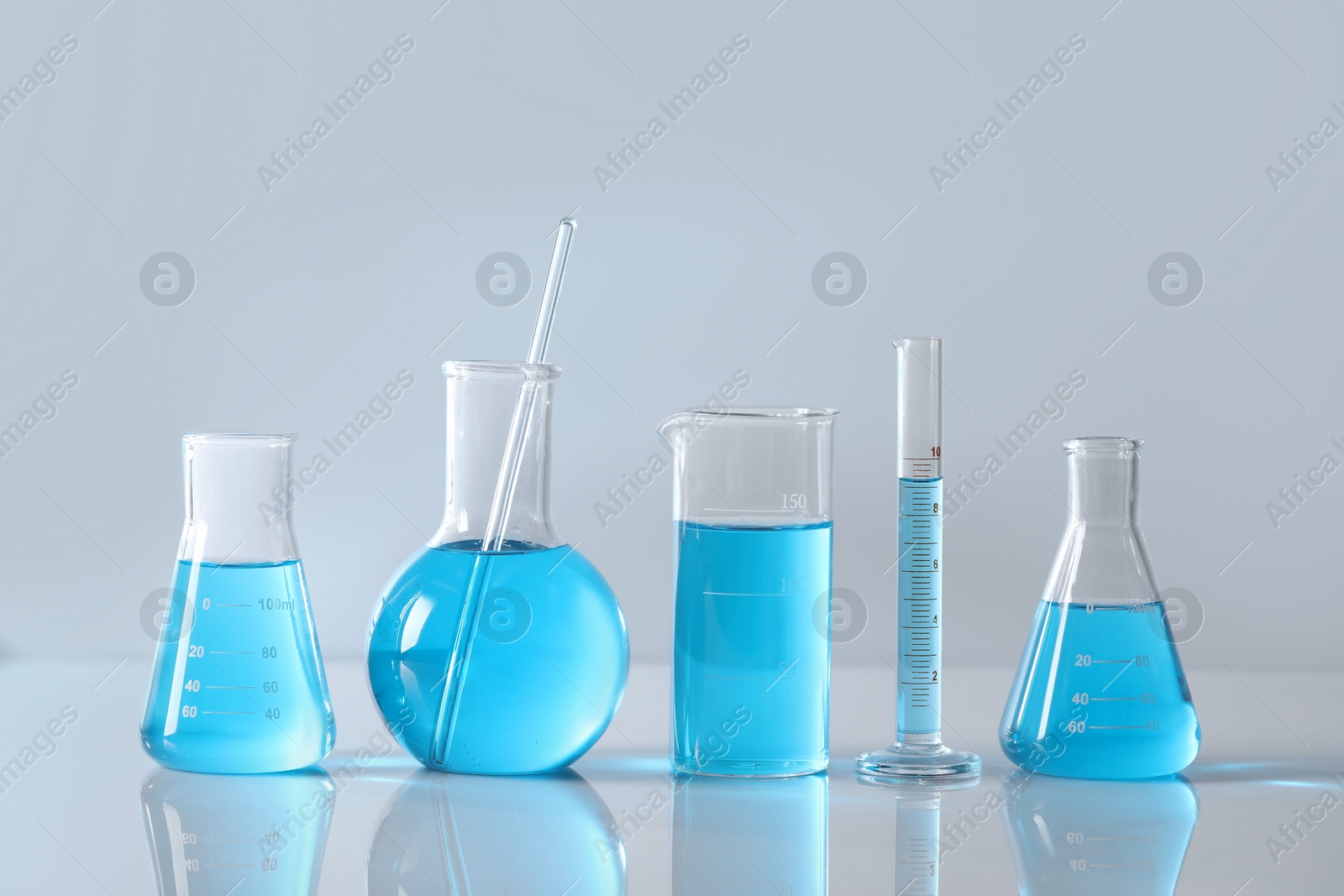 Photo of Different laboratory glassware with light blue liquid on table