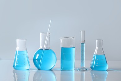 Different laboratory glassware with light blue liquid on table