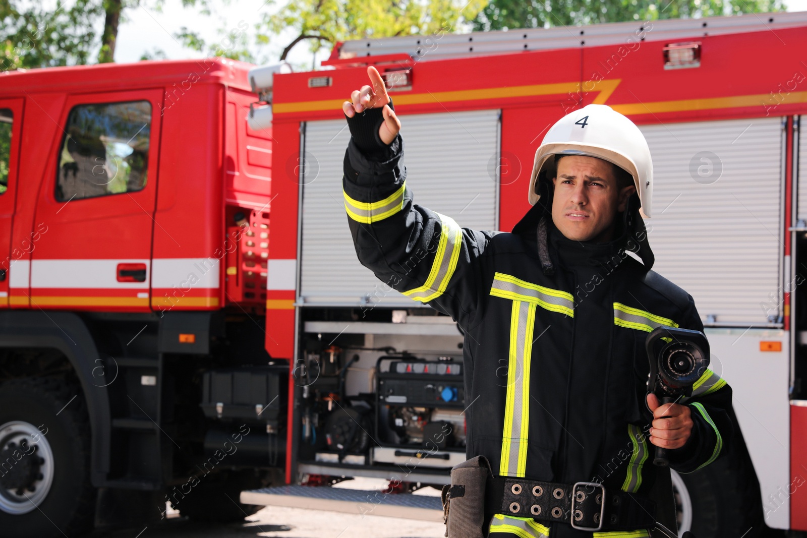 Photo of Firefighter in uniform with high pressure water jet near fire truck outdoors