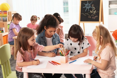 Photo of Adorable children drawing together at table indoors. Kindergarten playtime activities