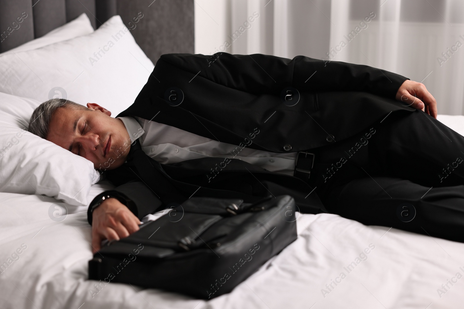 Photo of Businessman with briefcase sleeping on bed indoors