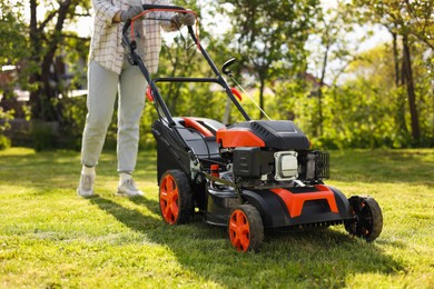 Woman cutting green grass with lawn mower in garden, selective focus