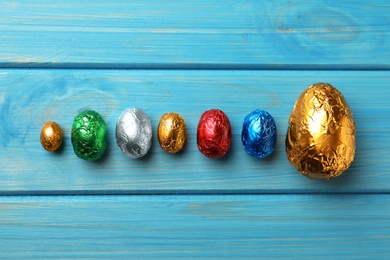 Chocolate eggs wrapped in colorful foil on light blue wooden table, flat lay