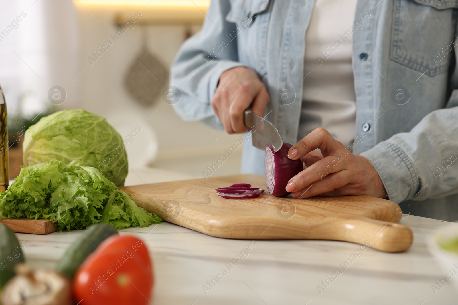 Photo of Woman cutting onion at white marble table in kitchen, closeup