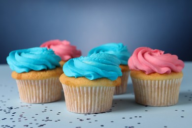 Photo of Delicious cupcakes with bright cream and confetti on blue background, closeup