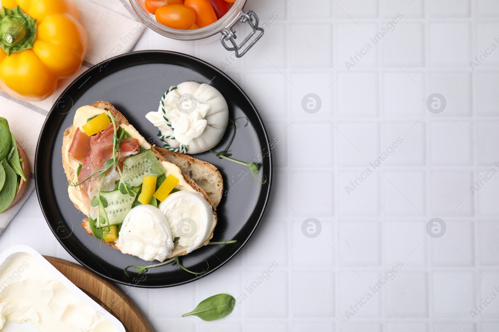 Photo of Tasty sandwich with burrata cheese, prosciutto, vegetables and ingredients on white tiled table, flat lay. Space for text