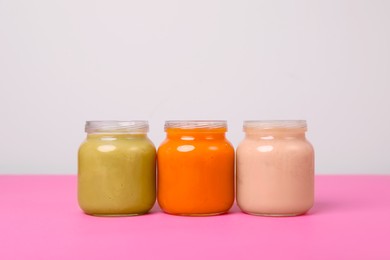 Photo of Glass jars with healthy baby food on pink table