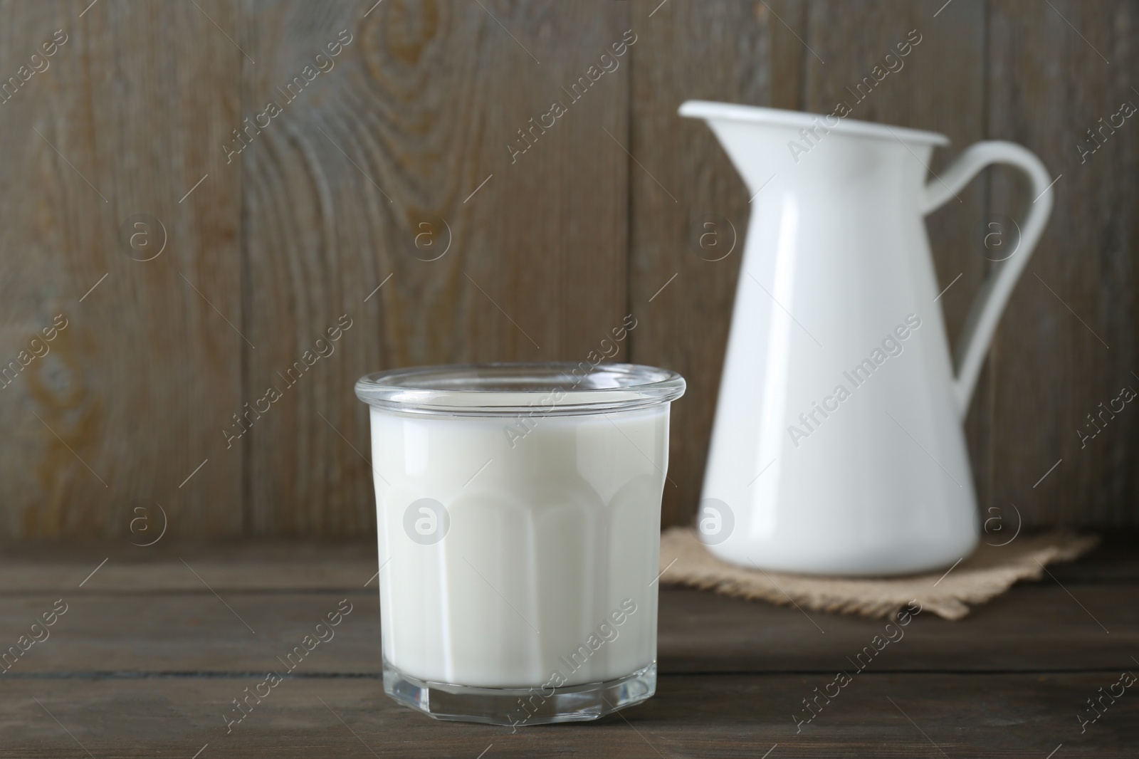 Photo of Glass of fresh milk and jug on wooden table, space for text