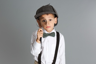 Little boy with magnifying glass playing detective on grey background