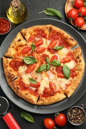 Photo of Delicious Margherita pizza, ingredients and cutter on black table, top view