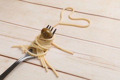 Photo of Heart made of tasty spaghetti, fork and olive on light wooden table. Space for text