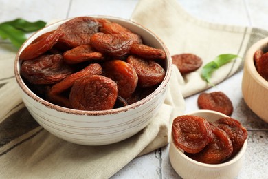 Photo of Tasty apricots in bowls on white tiled table, closeup. Dried fruits