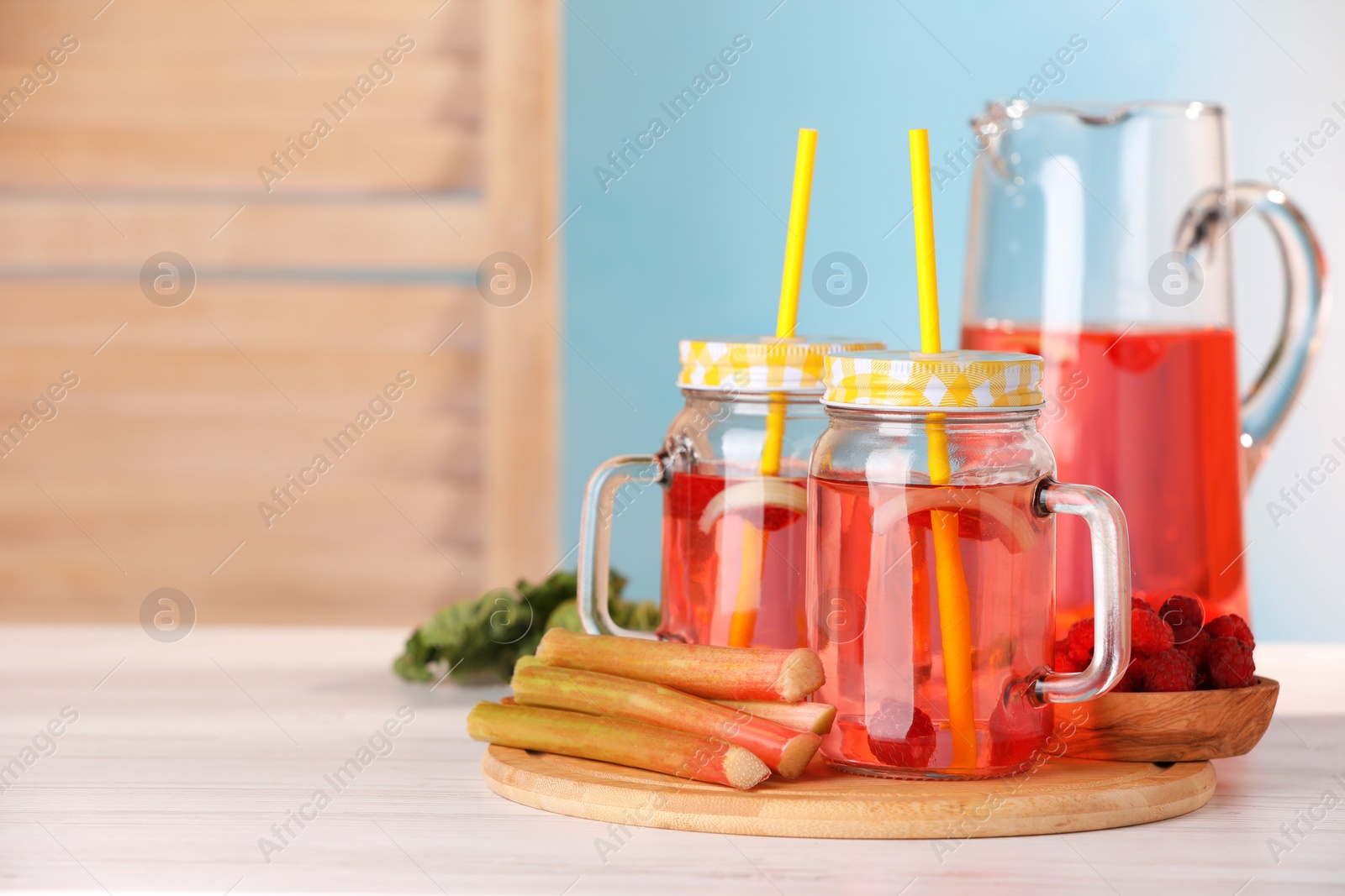Photo of Tasty rhubarb cocktail with raspberry and stalks on white table. Space for text