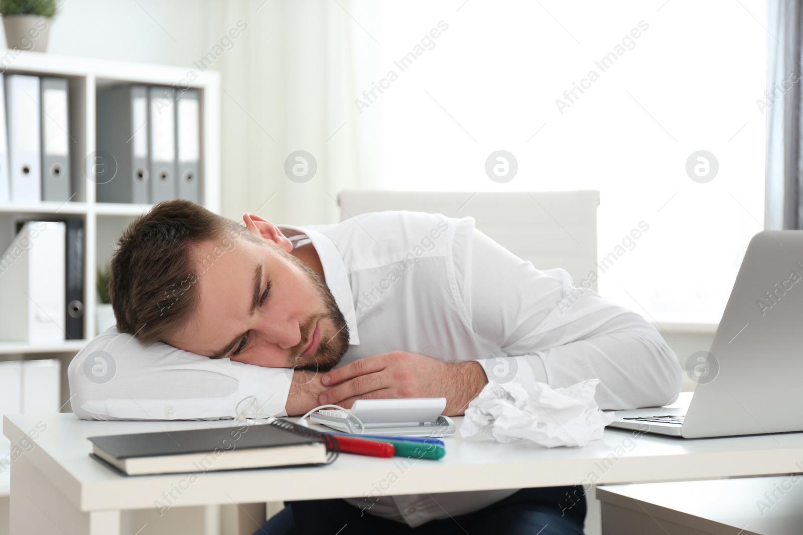 Photo of Lazy young man wasting time at messy table in office