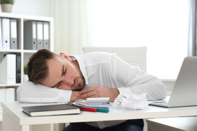 Lazy young man wasting time at messy table in office