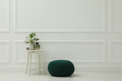 Photo of Knitted pouf and table with houseplants near white wall indoors. Space for text