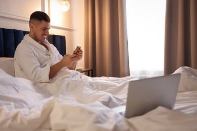 Photo of Handsome man using smartphone on bed in hotel room
