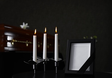 Photo of Black photo frame with burning candles on table in funeral home