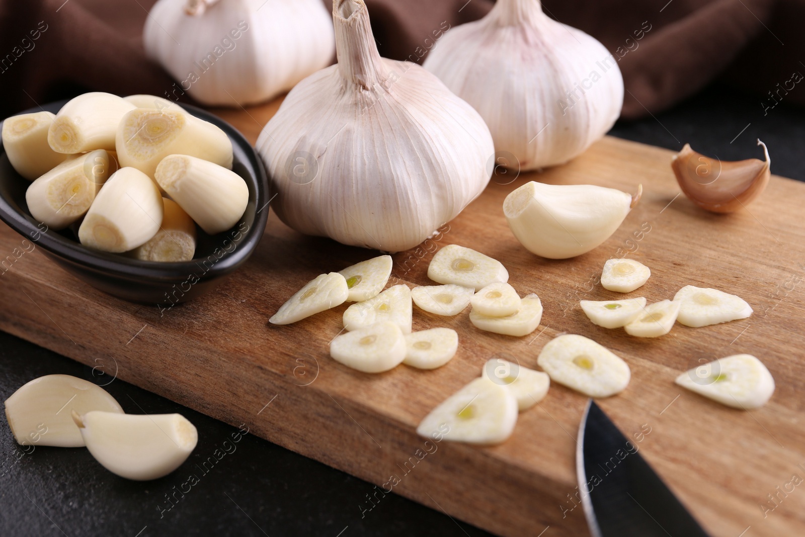 Photo of Aromatic cut garlic, cloves and bulbs on dark table, closeup