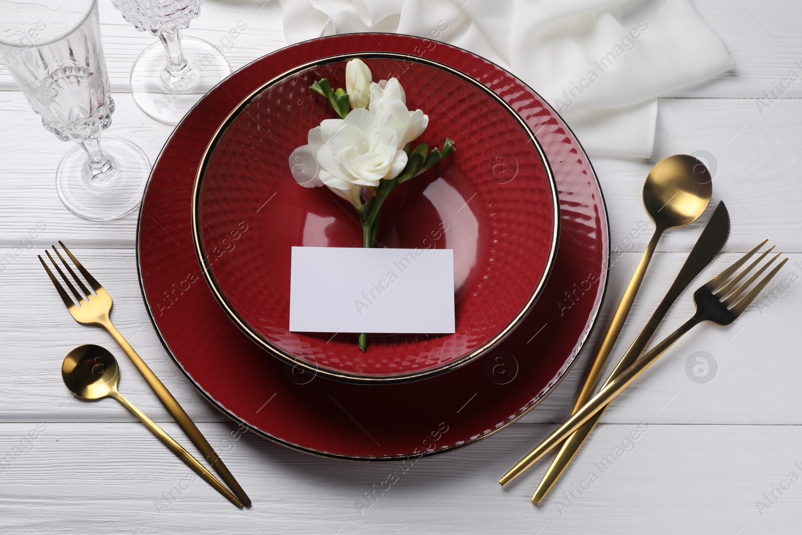 Photo of Stylish table setting. Dishes, cutlery, blank card and floral decor on white wooden background, above view