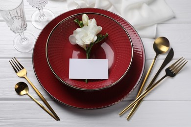 Stylish table setting. Dishes, cutlery, blank card and floral decor on white wooden background, above view