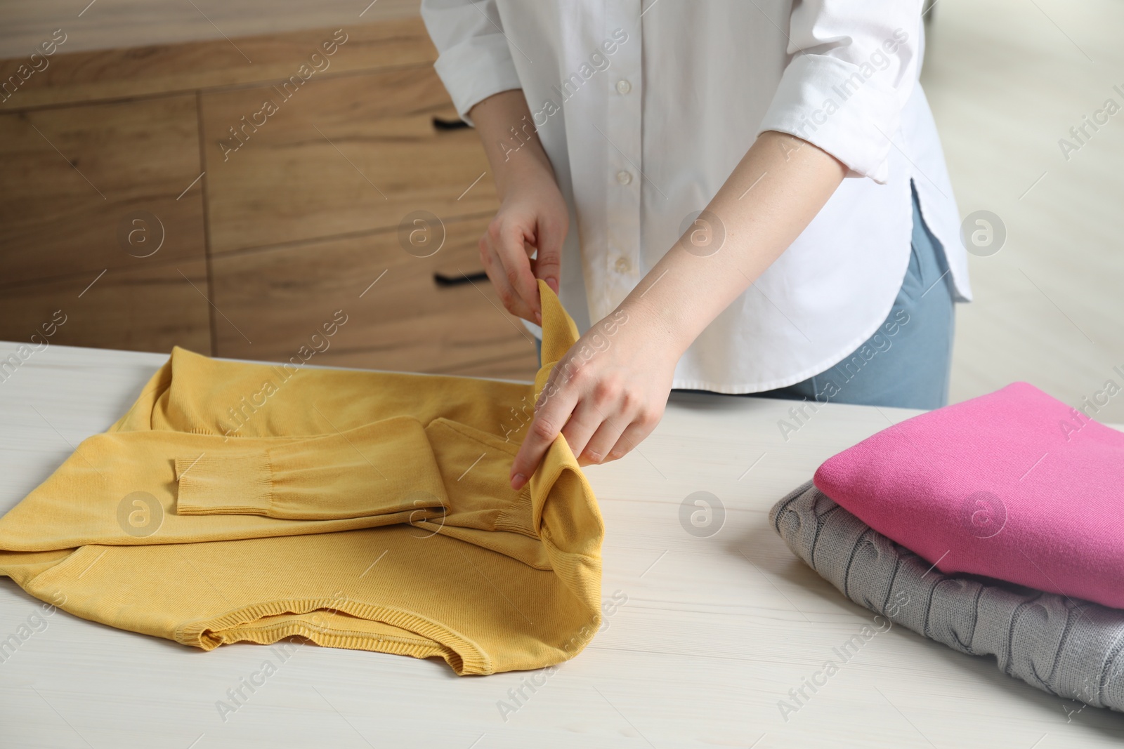 Photo of Woman folding clothes at white wooden table indoors, closeup