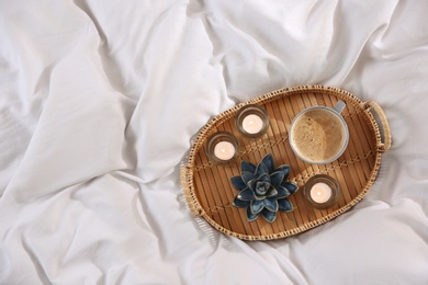 Photo of Wicker tray with cup of coffee and candles on soft white blanket, top view