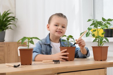 Photo of Cute little girl planting seedling into pot at wooden table in room
