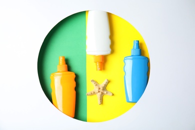 Photo of Bottles with sun protection products and starfish in round frame on color background, top view