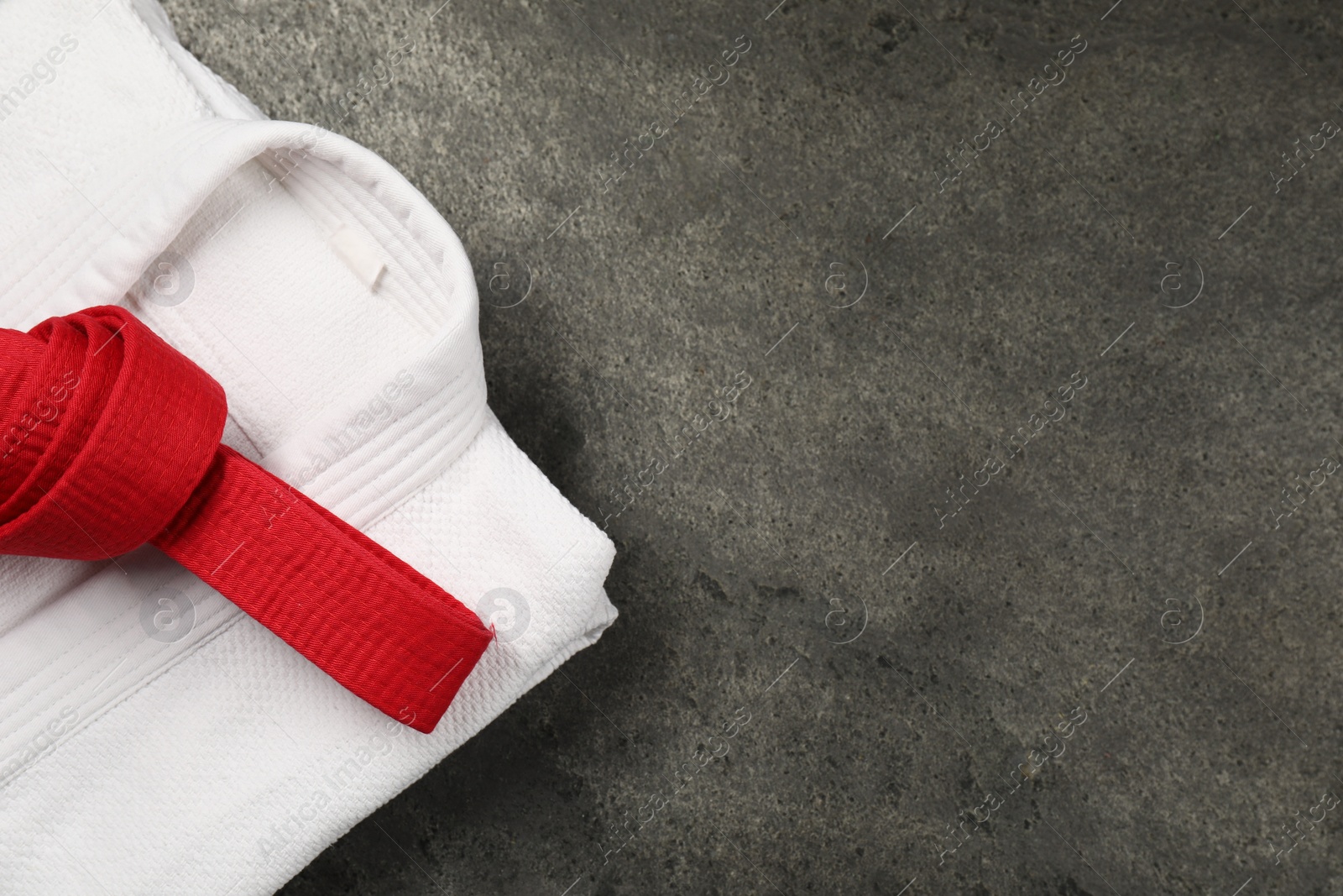 Photo of Red karate belt and white kimono on gray textured background, top view. Space for text