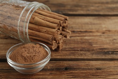 Aromatic cinnamon powder and sticks on wooden table, closeup. Space for text
