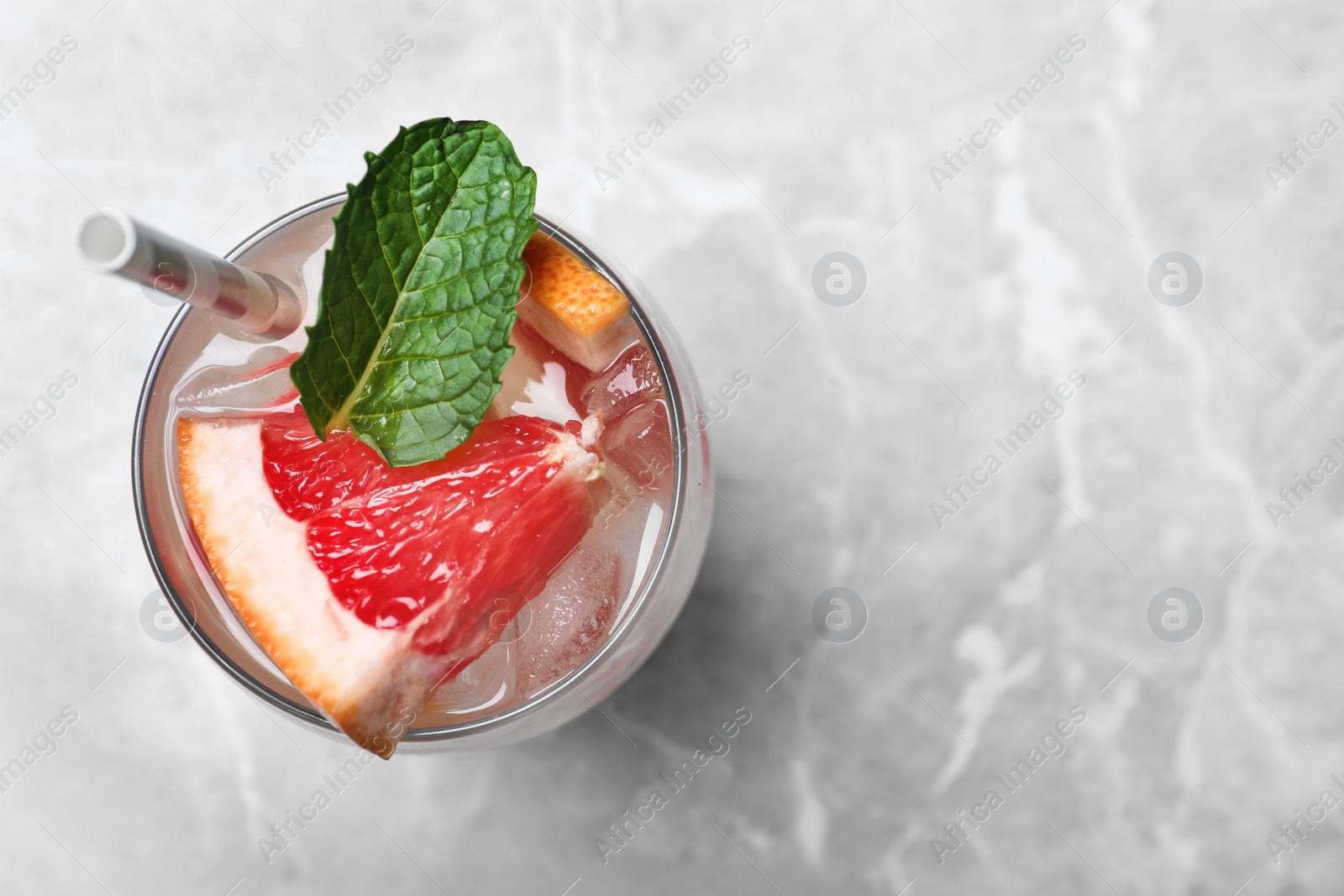 Photo of Glass of fresh cocktail with grapefruit on grey marble table, top view. Space for text