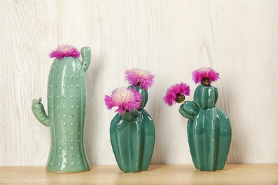 Photo of Trendy cactus shaped ceramic vases with flowers on table against wooden background