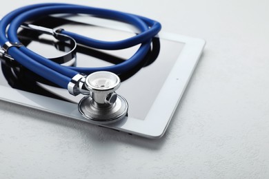 Photo of Computer tablet with stethoscope on white table, closeup. Space for text