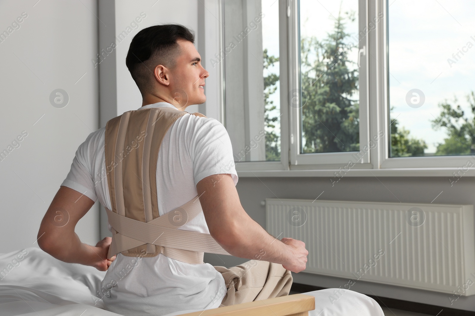 Photo of Handsome man with orthopedic corset sitting in bedroom