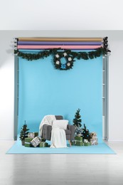 Photo of Beautiful Christmas themed photo zone with stylish armchair, trees and gift boxes in studio