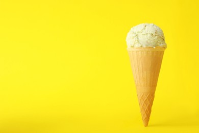 Photo of Delicious ice cream in waffle cone on yellow background. Space for text