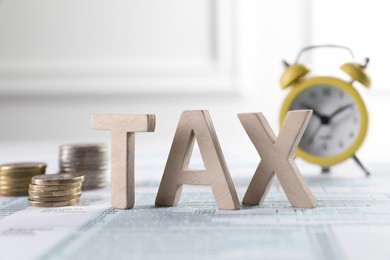 Word Tax made with wooden letters, coins and alarm clock on document against light background