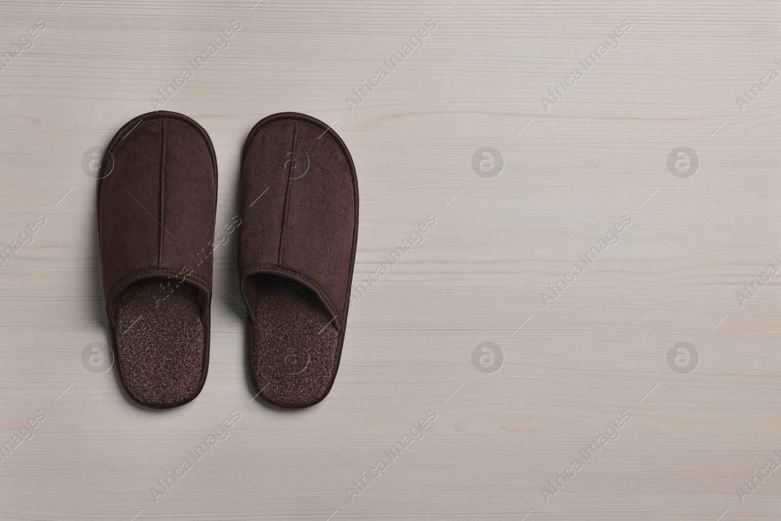 Photo of Pair of brown slippers on white wooden floor, top view. Space for text