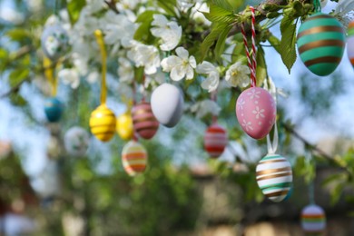 Beautifully painted Easter eggs hanging on blooming tree outdoors, space for text