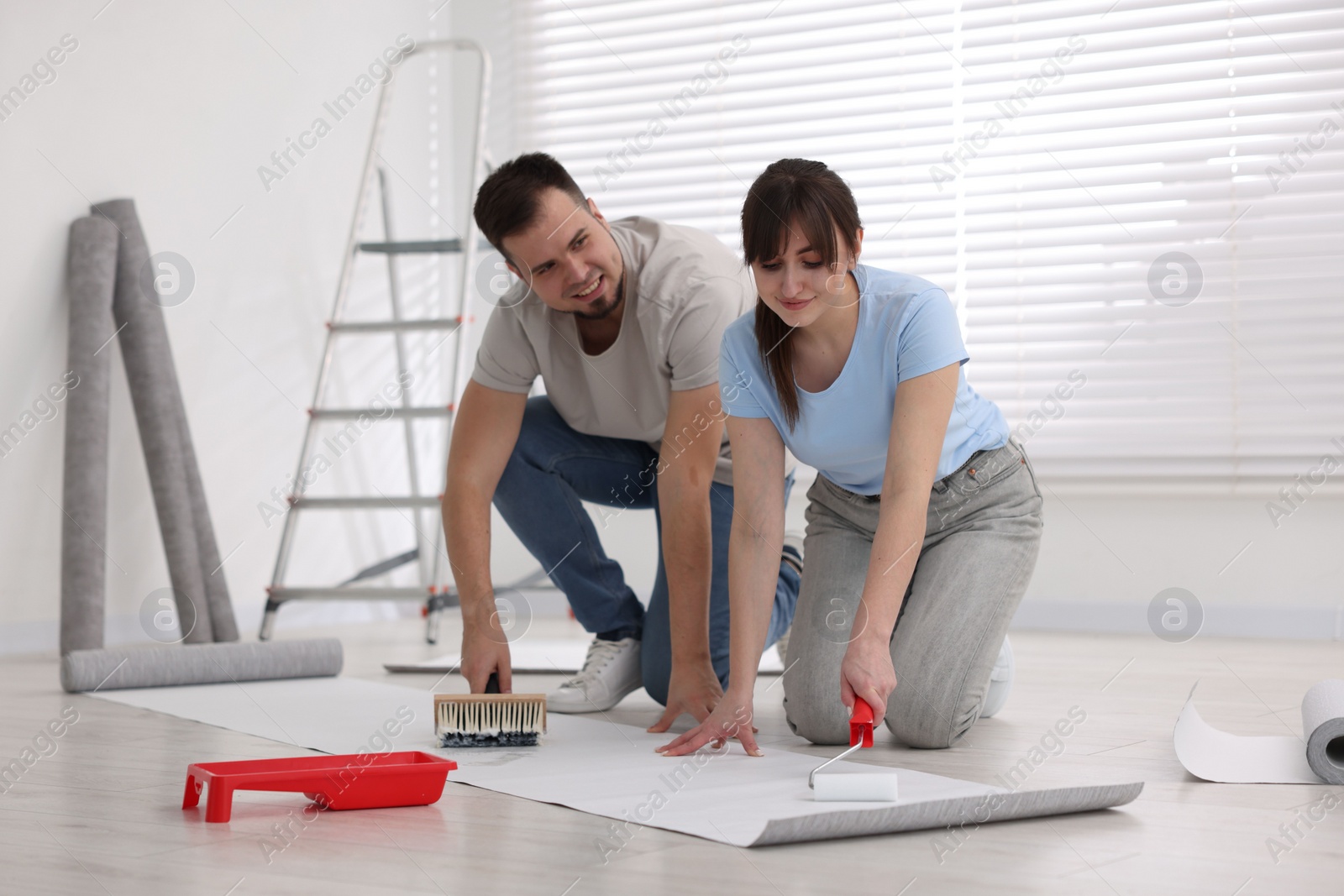 Photo of Couple applying glue onto wallpaper sheet in room