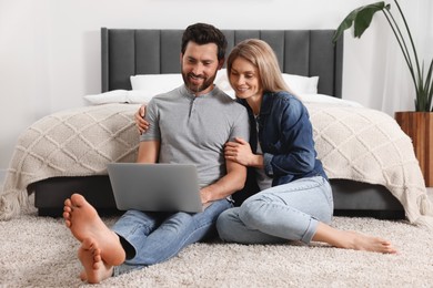 Photo of Happy couple with laptop on floor in bedroom