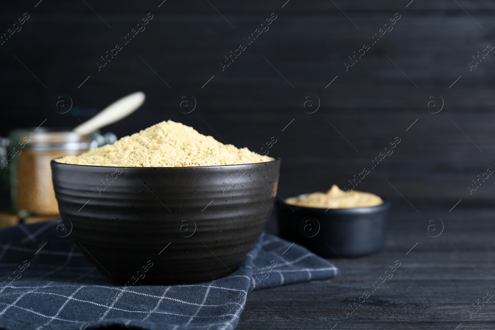 Photo of Bowl of aromatic mustard powder on black wooden table. Space for text