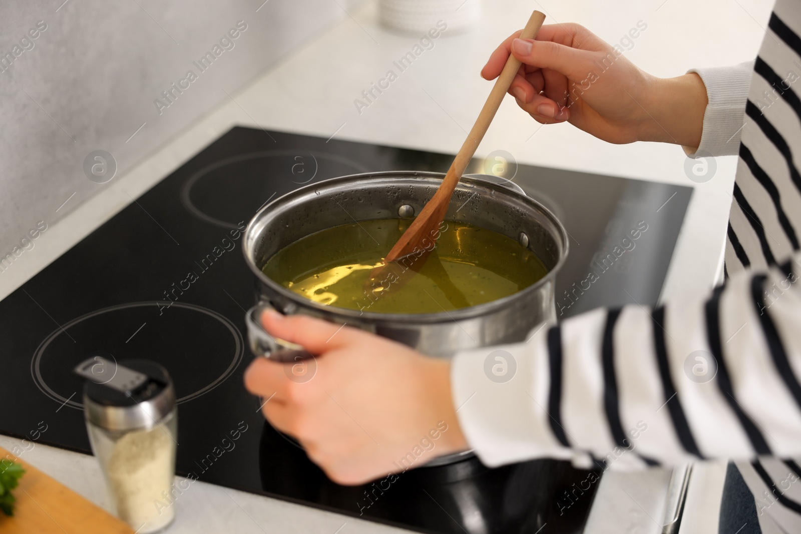 Photo of Woman with wooden spoon cooking soup in kitchen, closeup