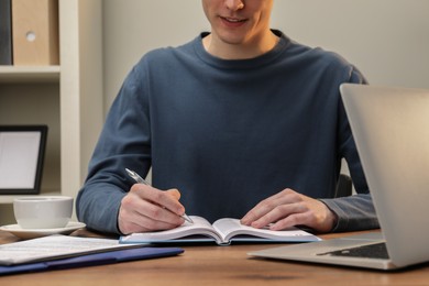 Man taking notes at wooden table in office, closeup