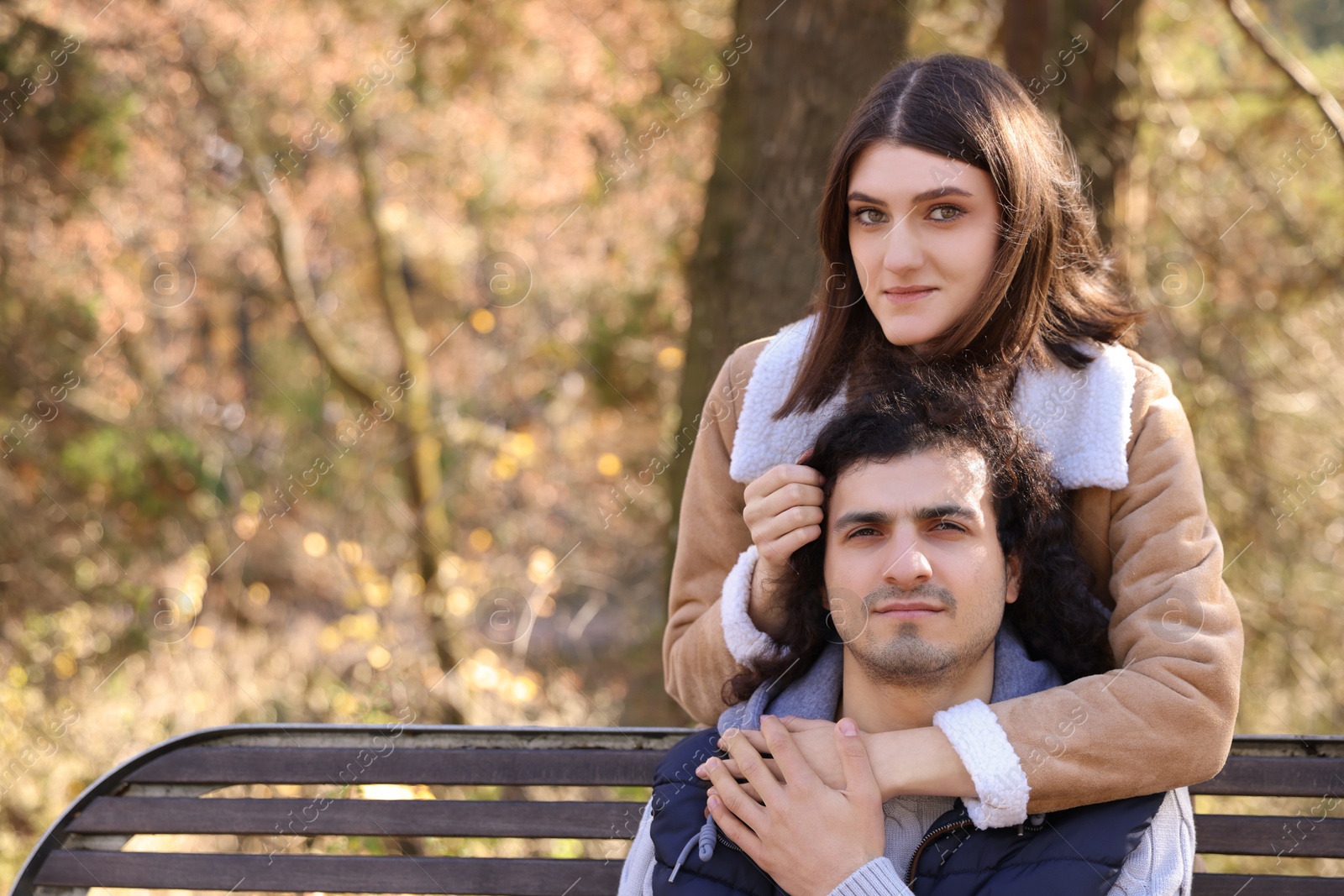 Photo of Young couple spending time together near wooden bench in autumn park, space for text. Dating agency