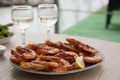 Photo of Plate of delicious cooked shrimps served with lemon and wine at table outdoors, closeup